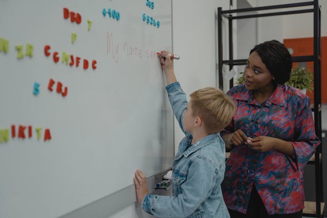 a teacher helping a student write on a whiteboard