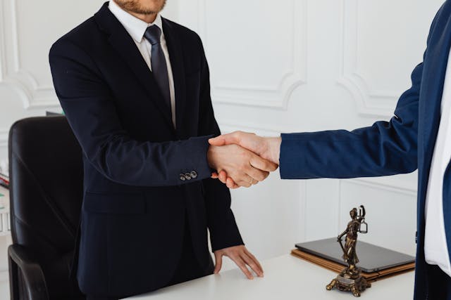 two people shaking hands in a lawyer's office with a small statue of Lady Justice between them