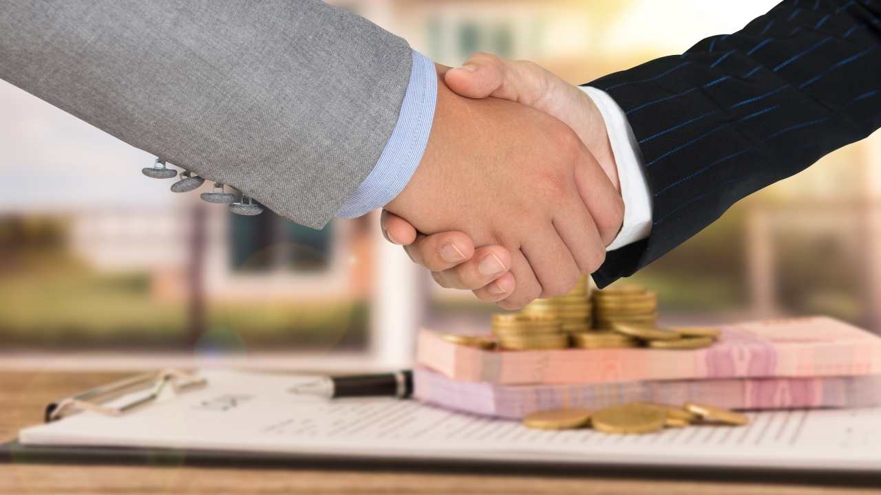 two people shaking hands with a contract and coins in the background